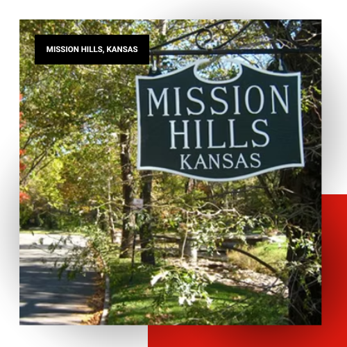 Green and white Mission Hills, Kansas welcome sign surrounded by trees and foliage along a residential street