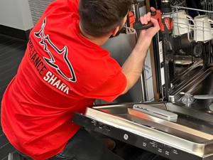 Appliance Shark technician in a red shirt repairing the interior of a stainless steel dishwasher