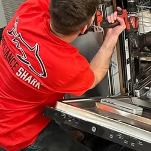 Appliance Shark technician in a red shirt using a power drill to repair the interior of a GE dishwasher