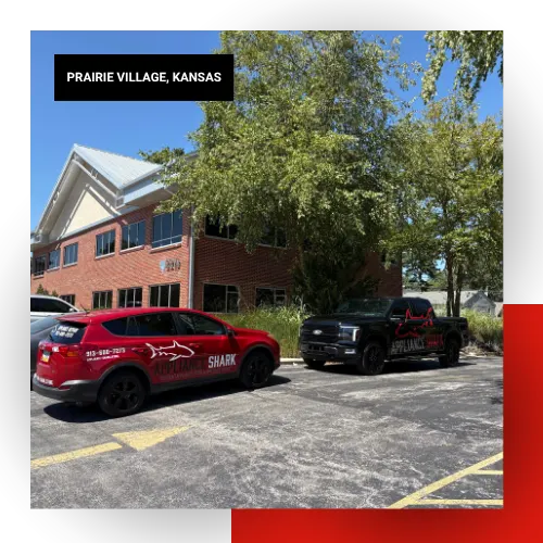 Appliance Shark branded red car and black truck parked outside a two-story brick office building in Prairie Village, Kansas