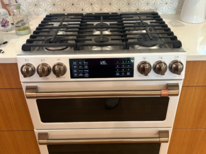 White Café brand double oven gas range with bronze knobs and a six-burner cooktop installed in a residential kitchen