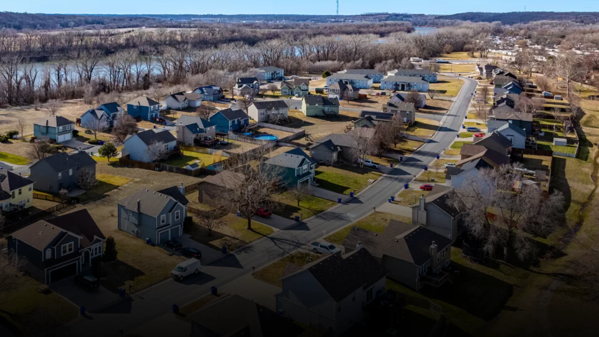 Aerial drone view of a residential neighborhood in Edwardsville, Kansas, with houses lining a winding street near a wooded riverbank