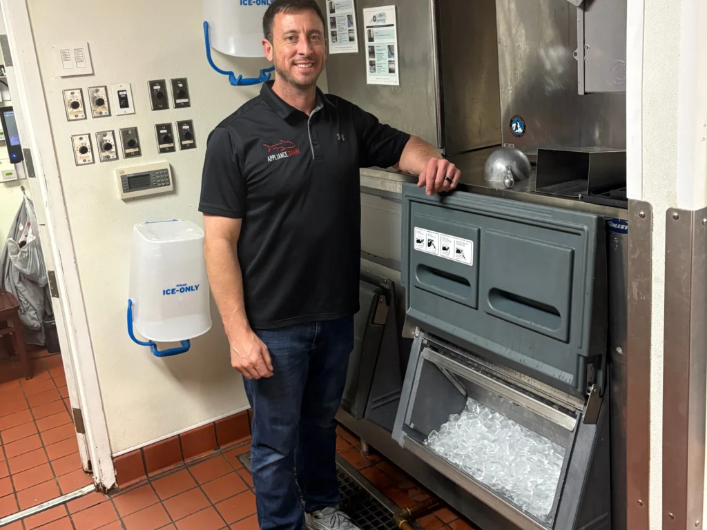 Appliance Shark technician standing beside a commercial ice machine, addressing an ice maker in freezer not working issue in a restaurant kitchen