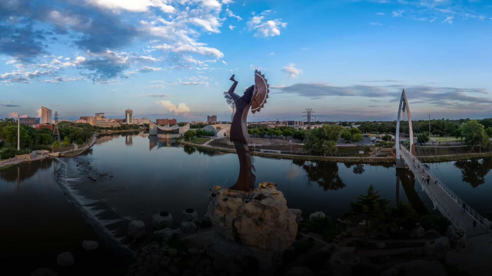 Keeper of the Plains statue overlooking the river confluence in Riverside, Wichita, Kansas, with the downtown skyline and pedestrian bridge in view