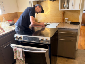 Technician in a black shirt repairing the stovetop of a stainless steel slide-in range in a residential kitchen