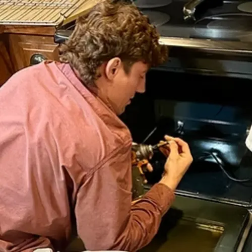 Technician in a pink shirt carefully repairing a component inside an open oven in a residential kitchen