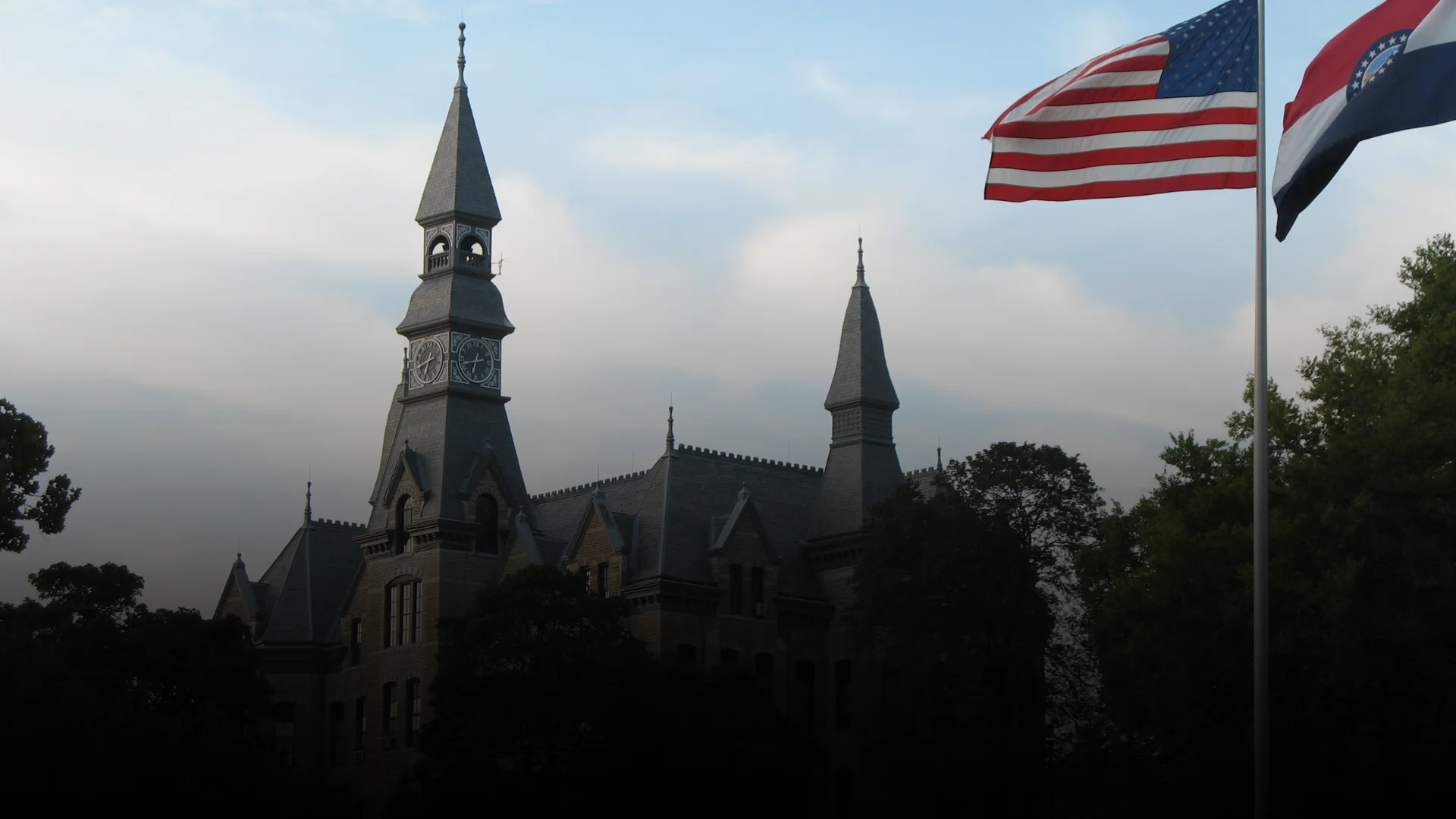 Historic clock tower building at Park University in Parkville, Missouri, silhouetted at dusk beside American and Missouri state flags