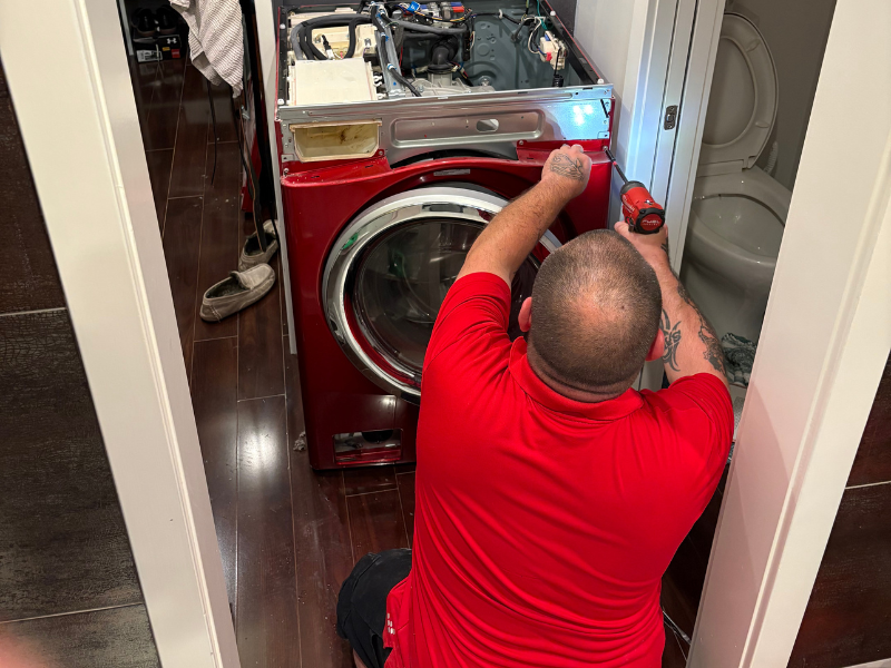 Appliance Shark technician repairing a red front-load washing machine in a home laundry closet