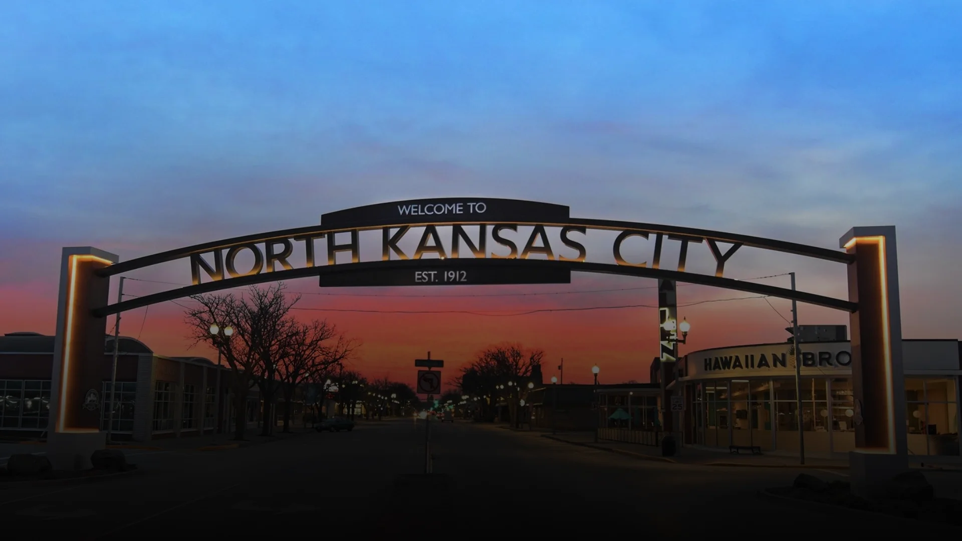Illuminated arch sign welcoming visitors to North Kansas City, established 1912, spanning the main street at sunset