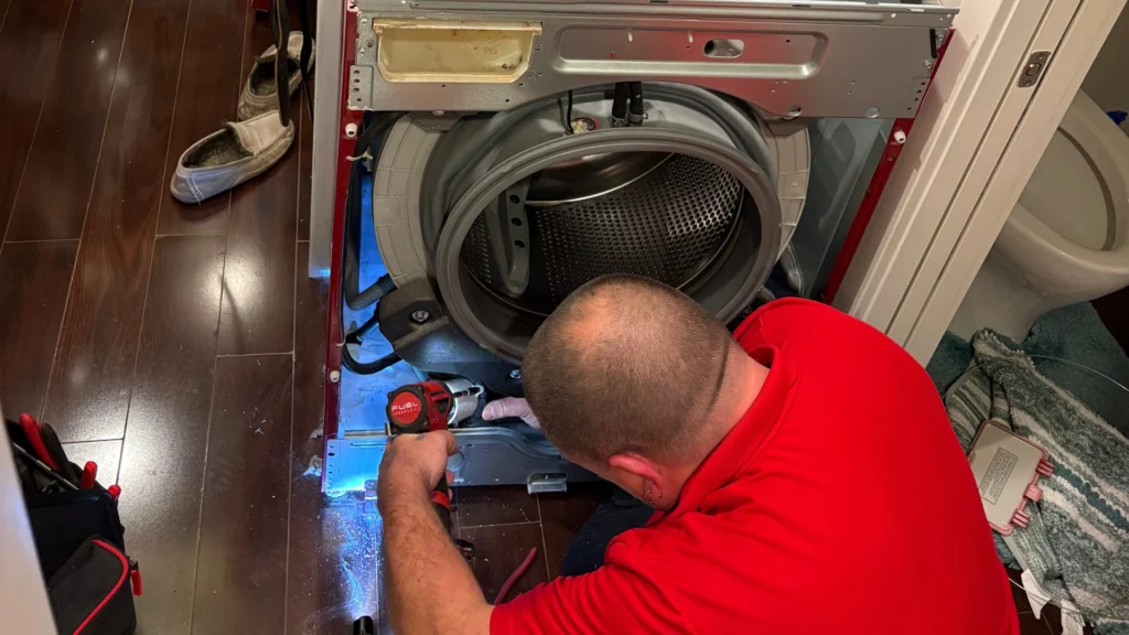 Technician using a power drill to repair the lower panel of a disassembled front-load washing machine